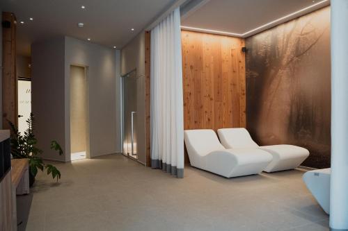 a living room with two white chairs and a wall at Mostesi Dolomites Spa Hotel in Auronzo di Cadore