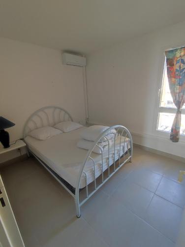 un lit blanc dans une chambre blanche avec une fenêtre dans l'établissement Cap d'Agde F3 belle vue port avec Garage Piscine Climatisation, au Cap d'Agde