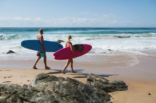 a man and woman walking on the beach with surfboards at Sala Beach House in Ballito