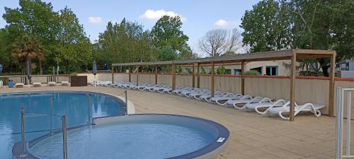 une piscine avec des chaises longues blanches et une clôture dans l'établissement Mobilhome L'Oasis Camping le Clos Cottet, à Angles