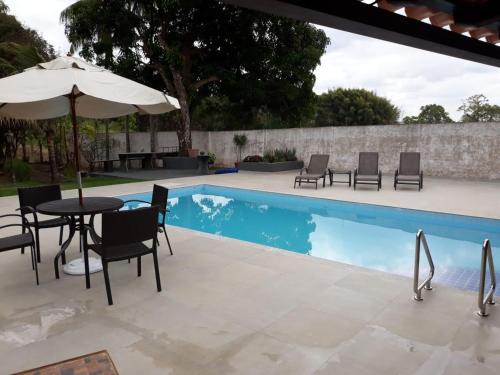 einen Pool mit einem Tisch, Stühlen und einem Sonnenschirm in der Unterkunft Rancho M, 5Qts - Lazer para sua família em Capitólio in Capitólio