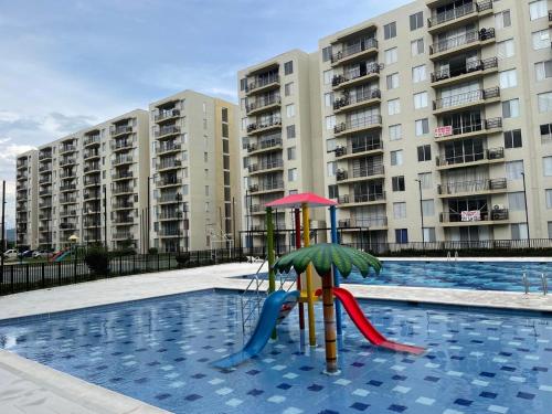 une piscine avec une aire de jeux devant des immeubles d'appartements dans l'établissement Acogedor apartamento, à Estación El Salto