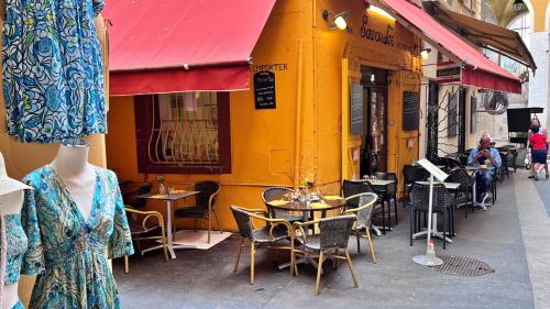 une femme passant devant un bâtiment jaune avec des tables et des chaises dans l'établissement Le Petit Niçois, à Nice