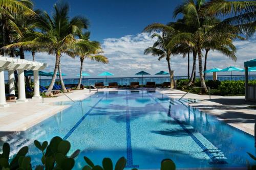 uma piscina com palmeiras e o oceano ao fundo em The Breakers Palm Beach em Palm Beach