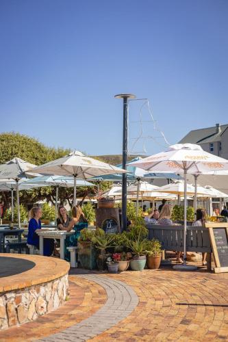 a group of people sitting at tables with umbrellas at Hermanus Waterfront Boho Studio Apartment, Whale Coast Hideaway in Hermanus