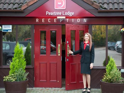a woman is standing in front of a red door at Peartree Lodge Waterside in Milton Keynes