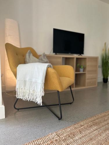 a living room with a yellow chair and a television at Boutique Townhouses Letterfrack Village - Entrance to Connemara National Park in Letterfrack