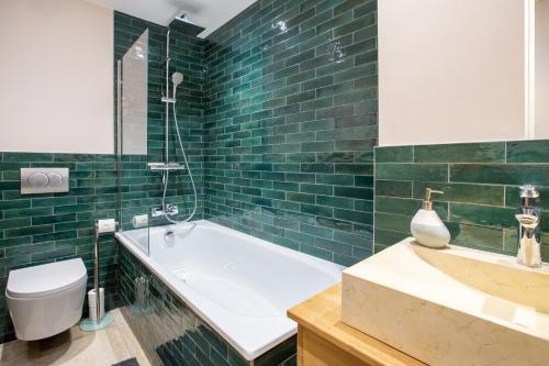 La salle de bains est pourvue de carrelage vert, d'une baignoire et de toilettes. dans l'établissement Large, bright and comfortable 3 bedroom apartment, à Morzine