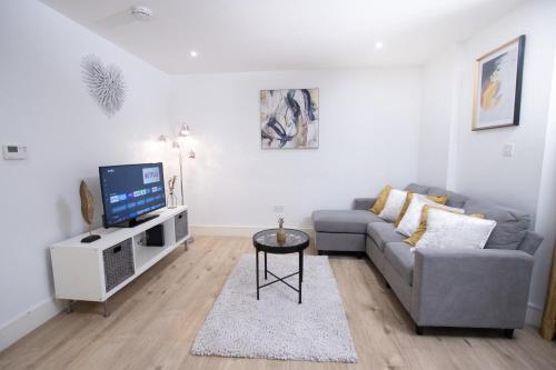 a living room with a gray couch and a tv at Midland Apartment I 1-min walk to town centre & station I 8-mins to airport I private balcony in Luton