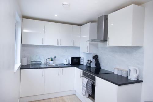 a kitchen with white cabinets and a black counter top at Midland Apartment I 1-min walk to town centre & station I 8-mins to airport I private balcony in Luton
