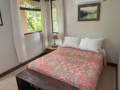 a bedroom with a bed with a colorful bedspread and two windows at Kakao Lodge & Garden Río Celeste in Bijagua