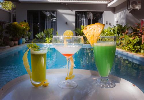 three drinks sitting on a table next to a pool at The L Boutique Tz in Dar es Salaam