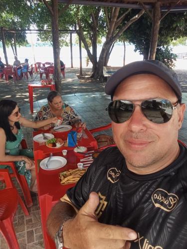 ein Mann mit Sonnenbrille und Hut sitzt an einem Tisch in der Unterkunft Casa Porto Maringá in Marilena