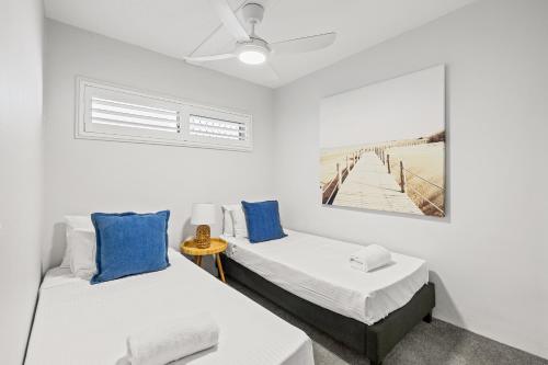 two beds in a white room with blue pillows at Maroochy Sands Holiday Apartments in Maroochydore