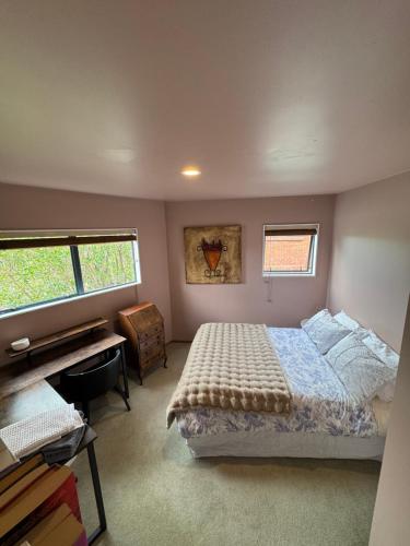 a bedroom with a bed and a desk and two windows at Sandy Toes & Netflix Nights, Relaxing Auckland Retreat in Auckland
