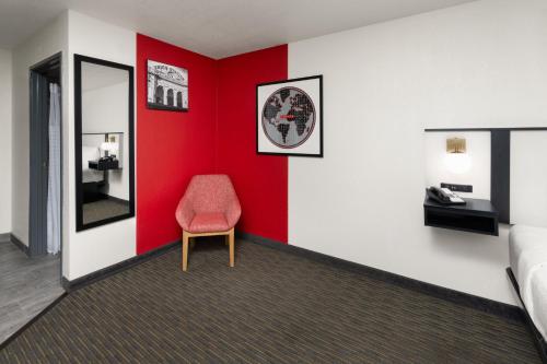 a red and white room with a chair and a mirror at SYLO Hotel Denver Airport, a Ramada by Wyndham in Aurora