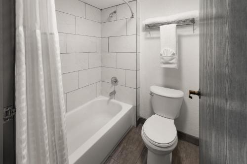 a bathroom with a toilet and a bath tub with a shower at SYLO Hotel Denver Airport, a Ramada by Wyndham in Aurora