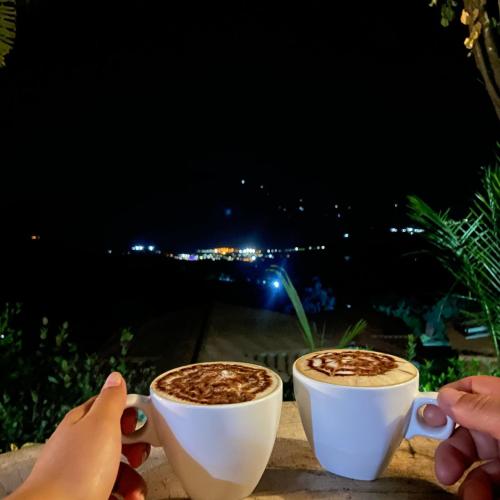 two people holding cups of coffee at night at cabañas campestres buena vista in Paicol