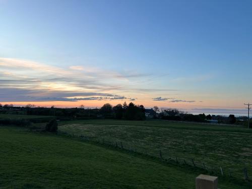 a field of grass with a sunset in the background at Fernlea Luxury Shepherds Hut & Hot Tub in Boosbeck