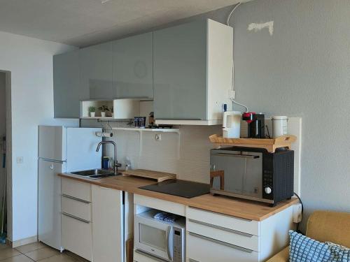 une petite cuisine avec des armoires blanches et un micro-ondes dans l'établissement Appartement T2 avec balcon vue port et accès piscine - FR-1-195-116, au Barcarès