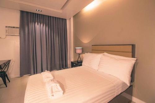 a bedroom with a bed with white sheets and a window at Aura Condotel in Roxas City