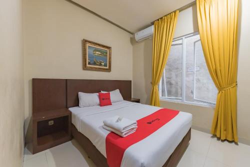 a bedroom with a bed and a window with yellow curtains at RedDoorz at La Mega near Pasar Pagi Cirebon in Cirebon