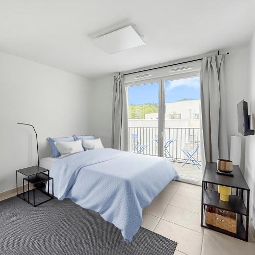 a white bedroom with a bed and a large window at Studio lumineux avec balcon privé in Poissy