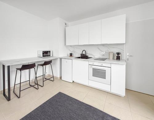 a kitchen with white cabinets and a counter with stools at Studio lumineux avec balcon privé in Poissy