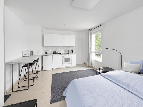 a white bedroom with a bed and a kitchen at Studio lumineux avec balcon privé in Poissy
