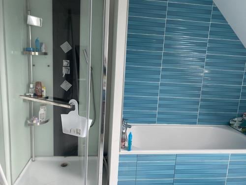 La salle de bains est pourvue d'une baignoire et d'une douche avec du carrelage bleu. dans l'établissement Maison récente au coeur du village historique, à Locronan