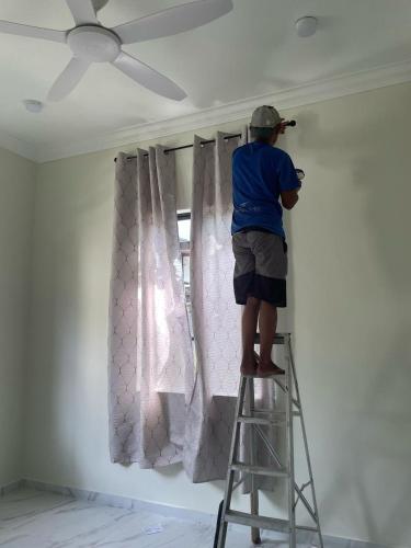 a man on a ladder painting a wall at Rumah Singgah in Kampong Tengah