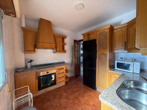 Una cocina con gabinetes de madera y un refrigerador negro. en Casa los Huertecillos, en Nívar