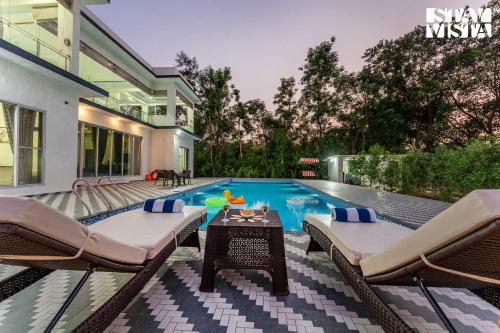 a swimming pool with chairs and a table next to a house at StayVista at Sky Hills with BBQ, Pool in Chinchavli
