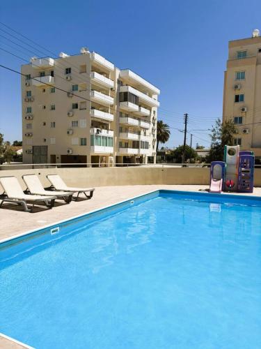a swimming pool with two lounge chairs and a building at 2BR Amalfi Blue Apt in Larnaca - Pool & 10Min Walk to Mackenzie Beach! in Larnaca