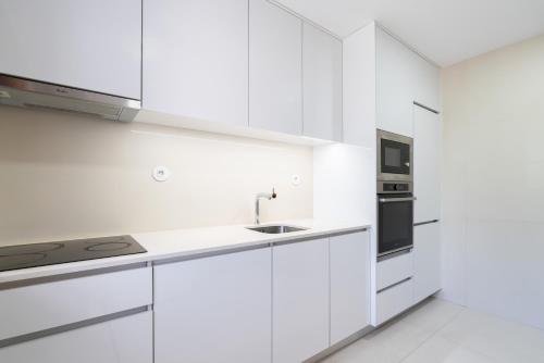 a white kitchen with white cabinets and a sink at Bright & Spacious Flat by Host Wise in Porto