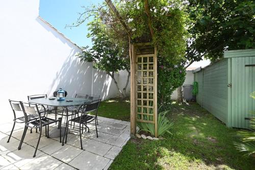 une table et des chaises assises sous un arbre dans une cour dans l'établissement 520 Le Petit Phare Village House, à Saint-Clément-des-Baleines