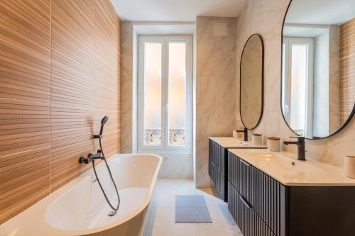 La salle de bains est pourvue d'une baignoire, de 2 lavabos et d'un miroir. dans l'établissement Charme et confort - centre ville de Nice, à Nice