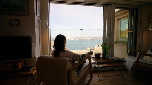 a young girl sitting in a chair looking out a window at Breathtaking Harbourside Views With Parking at 'Harbour Strand' in Falmouth