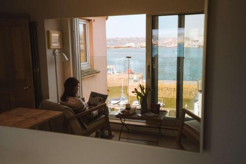 a woman sitting in a chair with a laptop in front of a window at Breathtaking Harbourside Views With Parking at 'Harbour Strand' in Falmouth