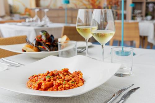 a table with a plate of food and two glasses of wine at Mercure Olbia in Olbia