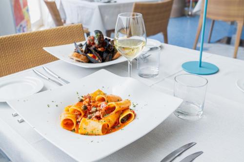 a table with a plate of pasta and a glass of wine at Mercure Olbia in Olbia