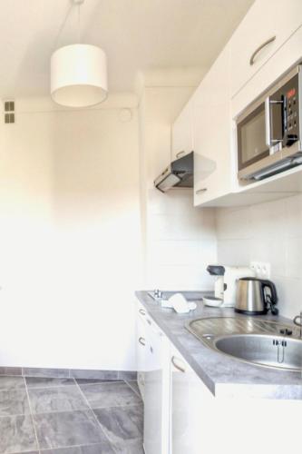 une cuisine blanche avec un évier et un micro-ondes dans l'établissement Grand Studio proche Croisette, à Cannes