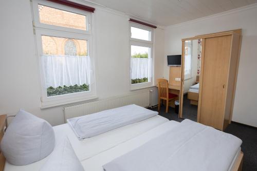 a bedroom with two beds and a desk and two windows at Hotel Zur Linde in Meldorf