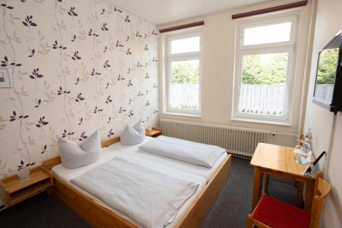 a small bedroom with a bed and two windows at Hotel Zur Linde in Meldorf