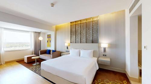 a hotel room with a white bed and a chair at Radisson Gurugram Udyog Vihar in Gurgaon