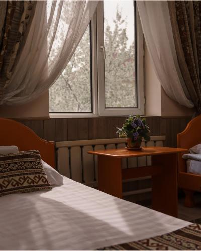 a bedroom with a bed and a table and two windows at Alpinist Hotel in Bishkek