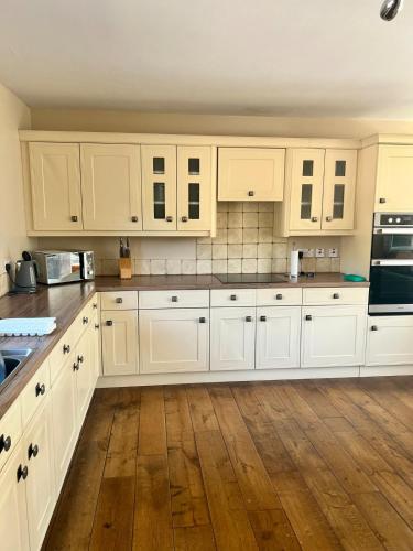 a kitchen with white cabinets and a wooden floor at Clianba- 3 bedroom Highland home from home in Spean Bridge