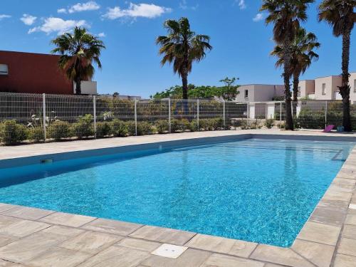 une piscine bleue avec des palmiers en arrière-plan dans l'établissement Villa 3 Ch. avec Jardin, Piscine, Parking et Plage à 400m – Sète - FR-1-472-151, à Sète