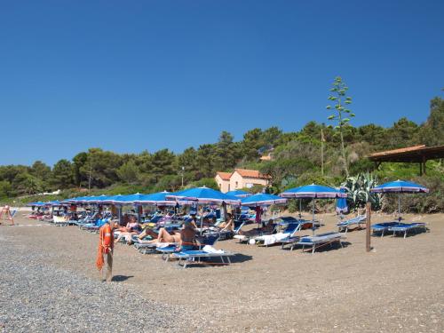 a group of people sitting on a beach with blue umbrellas at Hotel Capo Sud in Lacona