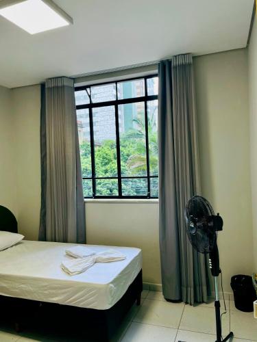 a room with a bed and a window with a fan at Belô Home & Office in Belo Horizonte